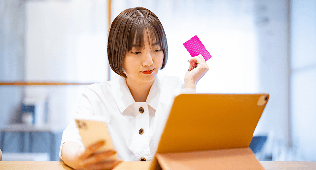 タブレットを見ながらスマホとクレジットカードを持つ女性
